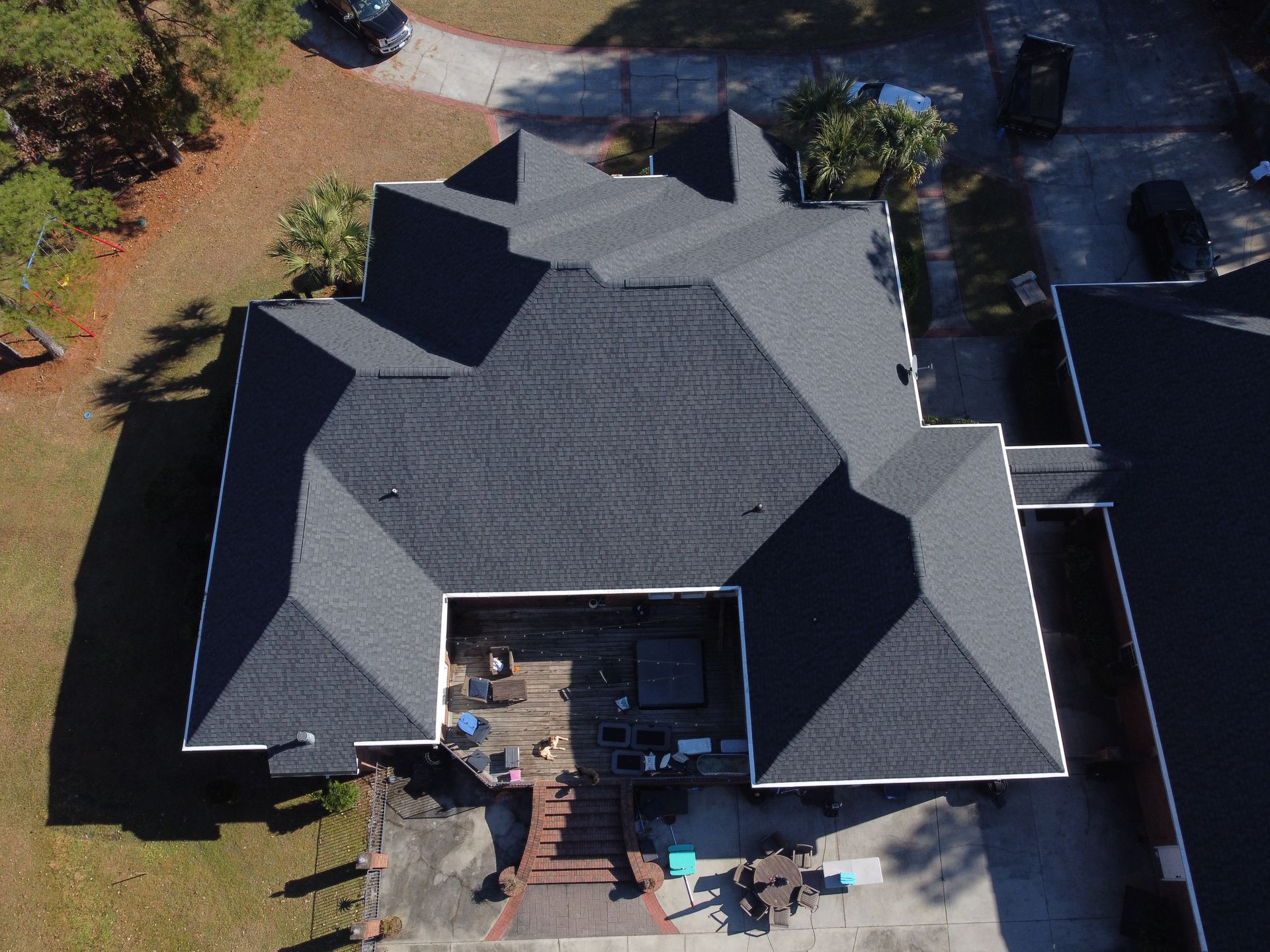 Overhead view of a house with a dark gray shingle roof. A patio is visible below.