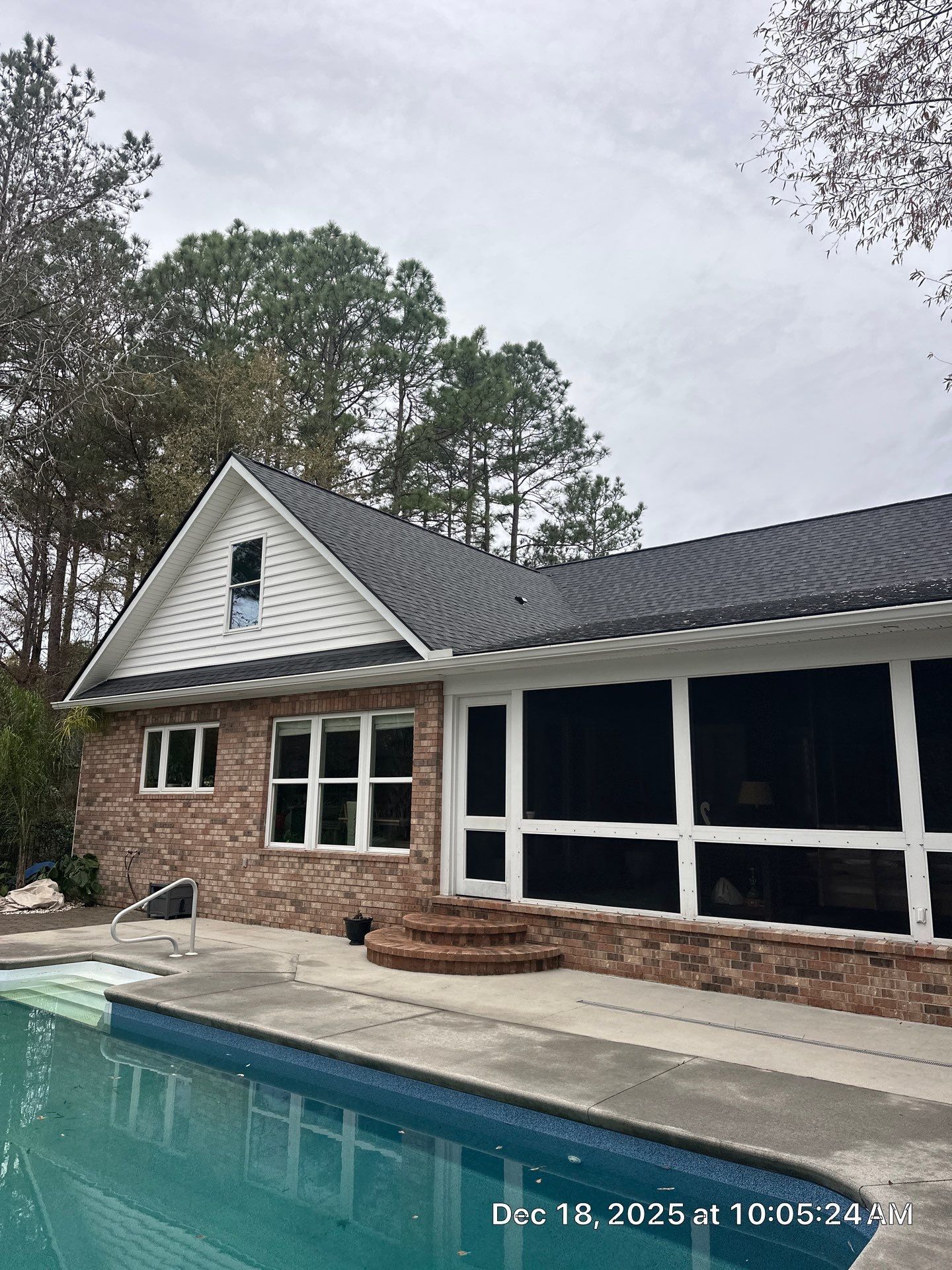 Brick house with a screened porch and swimming pool. Overcast sky.
