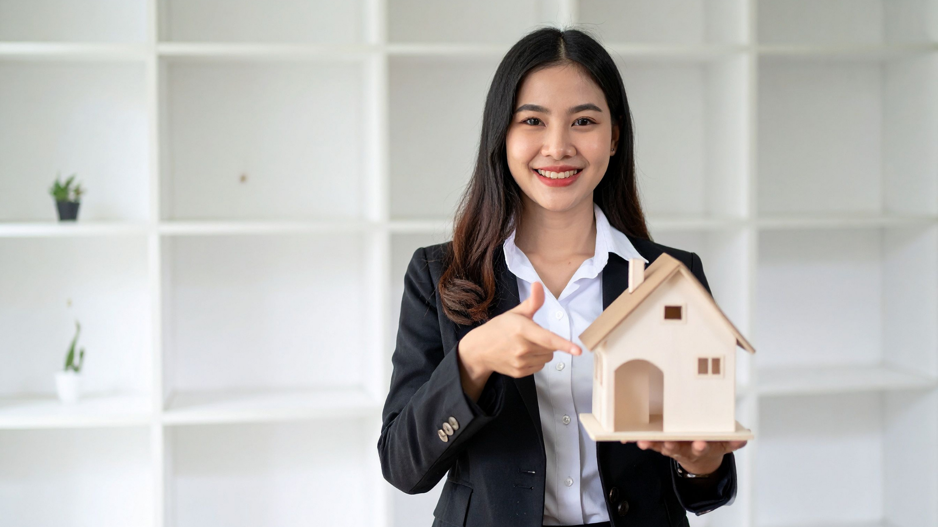 Smiling businesswoman holding a small house model in a bright office