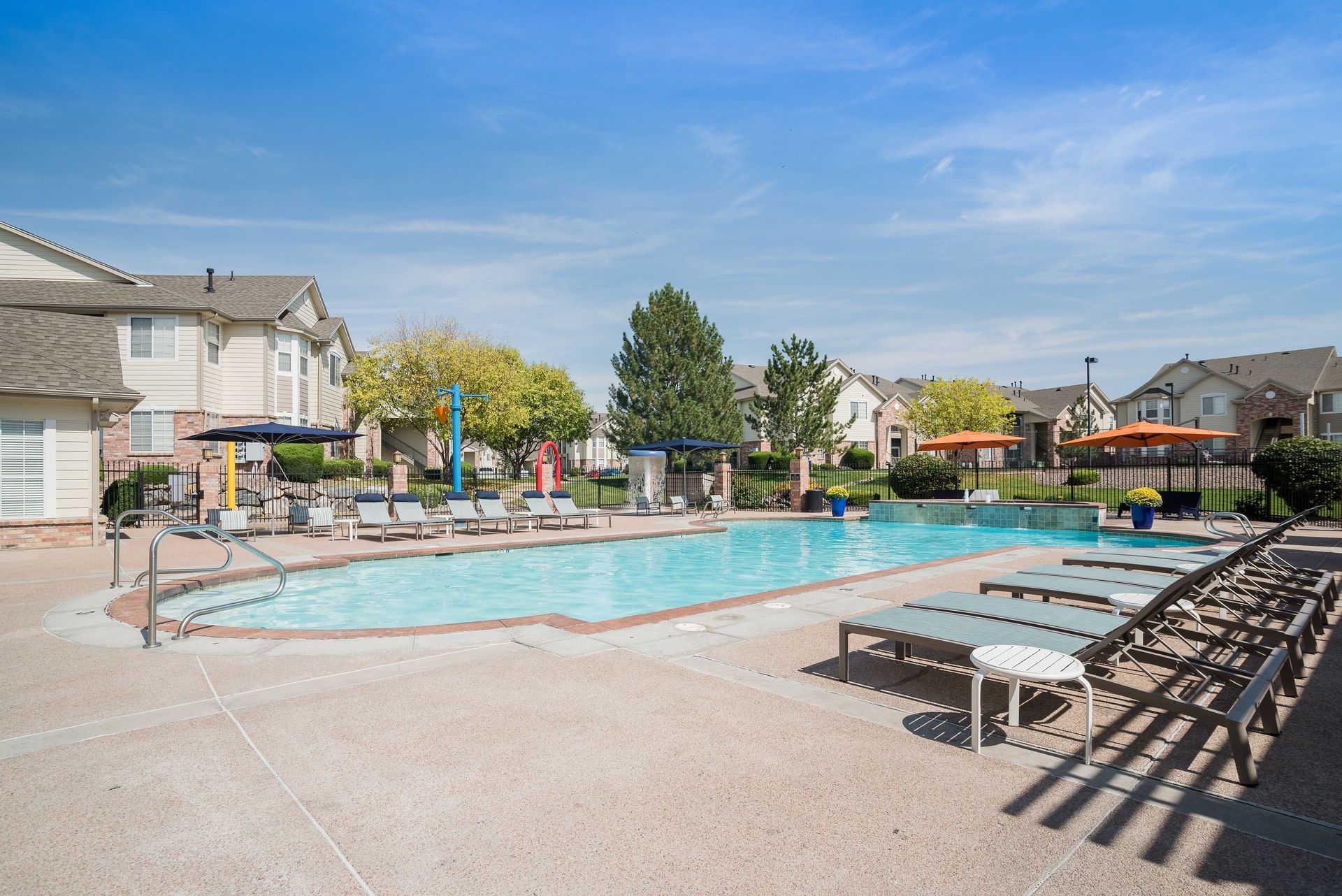 Swimming pool surrounded by lounge chairs and residential buildings under a blue sky.