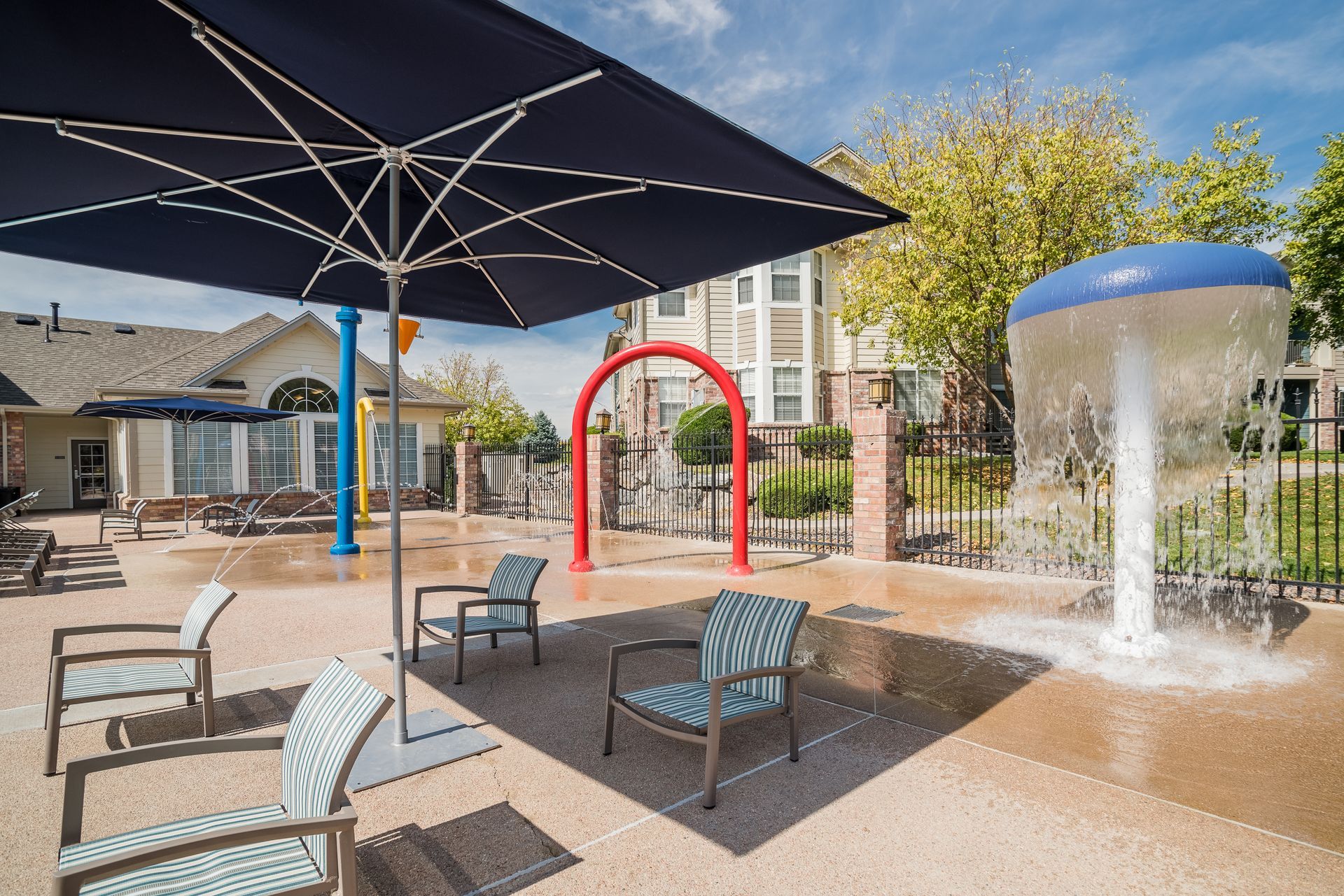 Splash pad with blue umbrella, chairs, and water feature.
