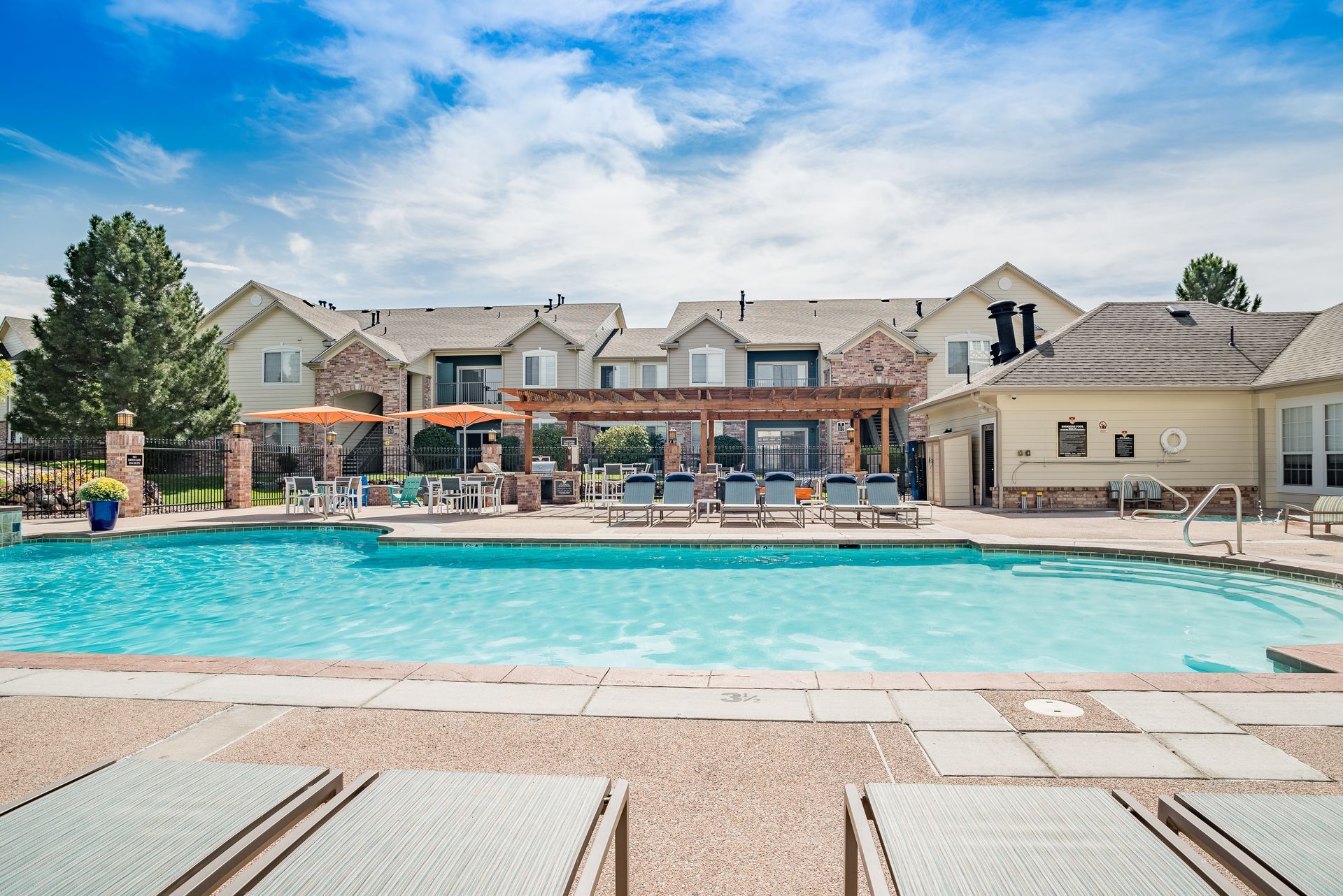 Swimming pool with lounge chairs in front of apartments, sunny day.