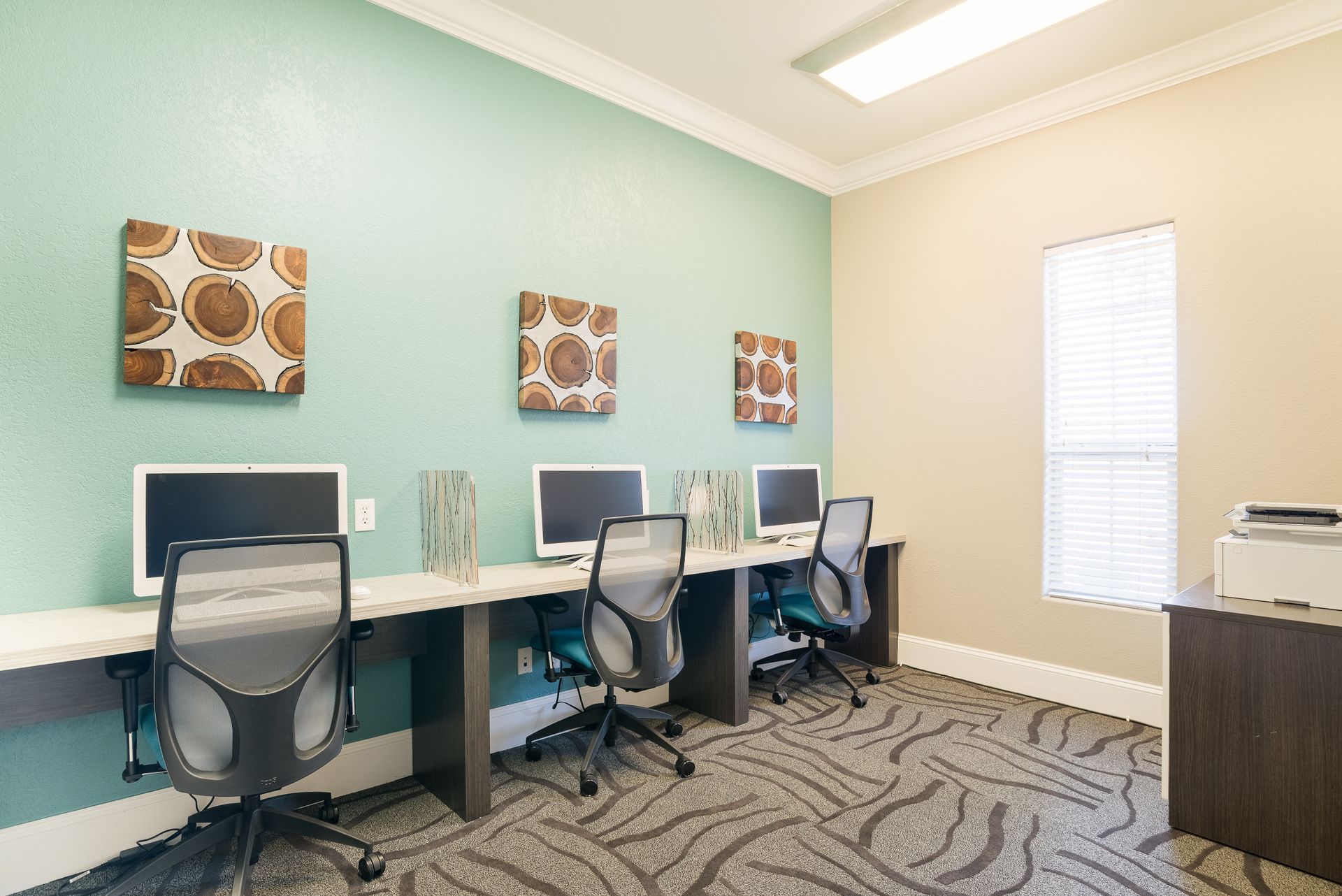 Office with computers and chairs; light green wall, beige wall, patterned carpet.