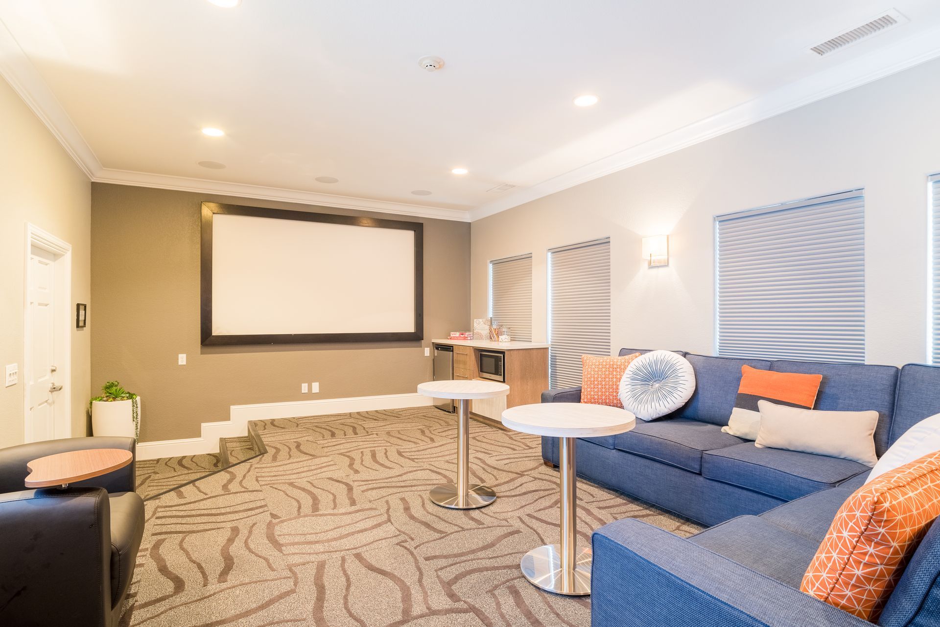 Cozy media room with blue sectional sofa, projection screen, and small tables.