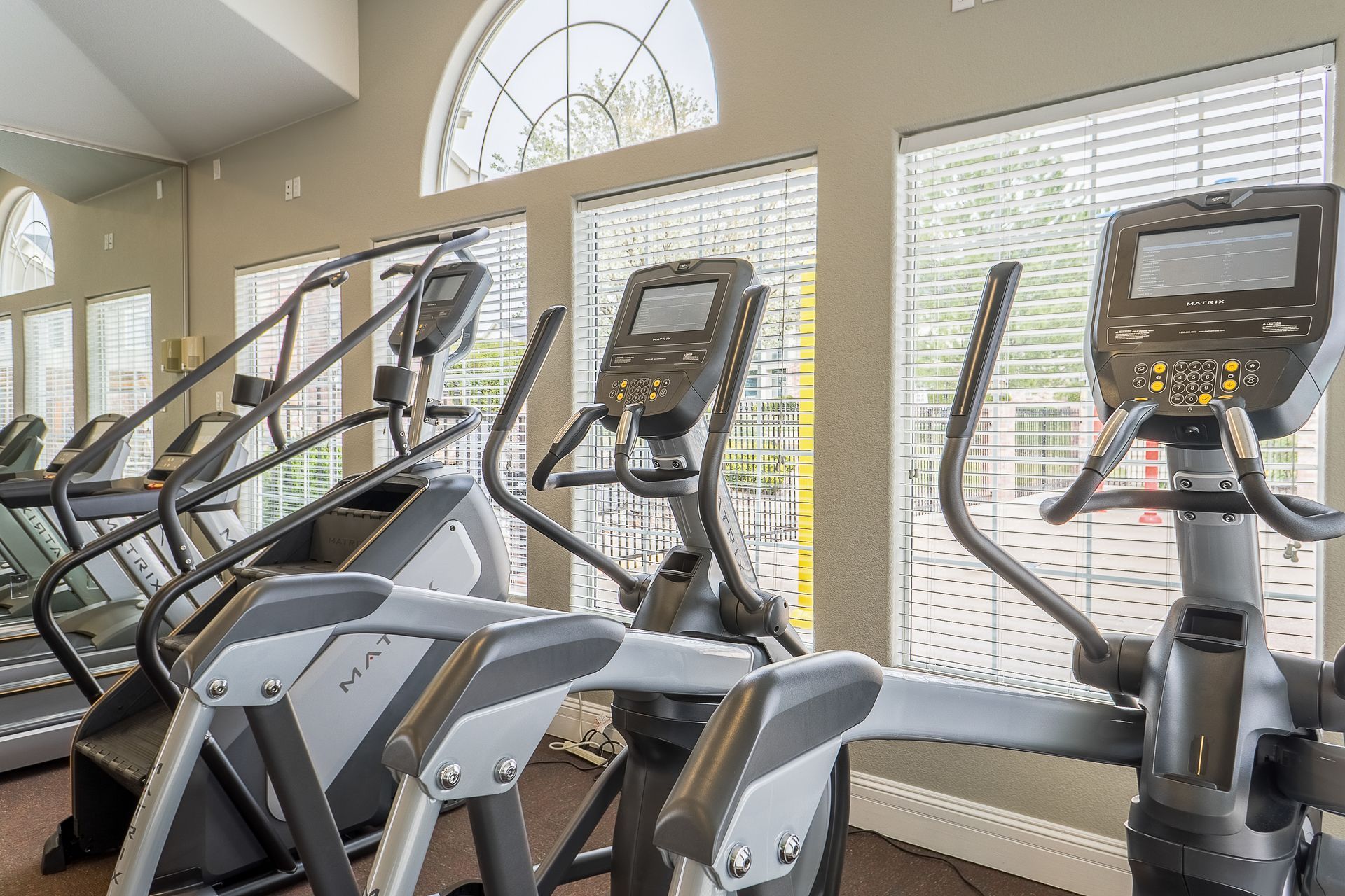 Gym with elliptical machines and a stair climber by windows.