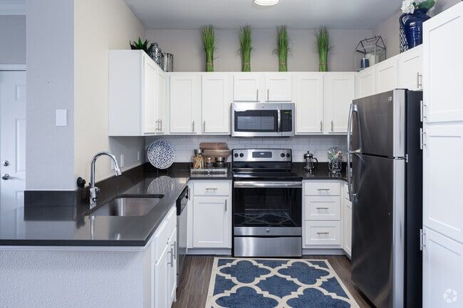 Bright kitchen with white cabinets, dark countertops, stainless steel appliances, and a blue patterned rug.