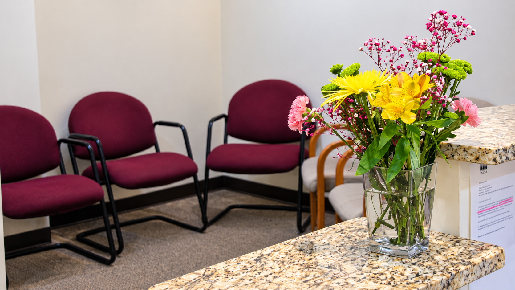 Waiting room with maroon chairs and a vase of colorful flowers on a marble table