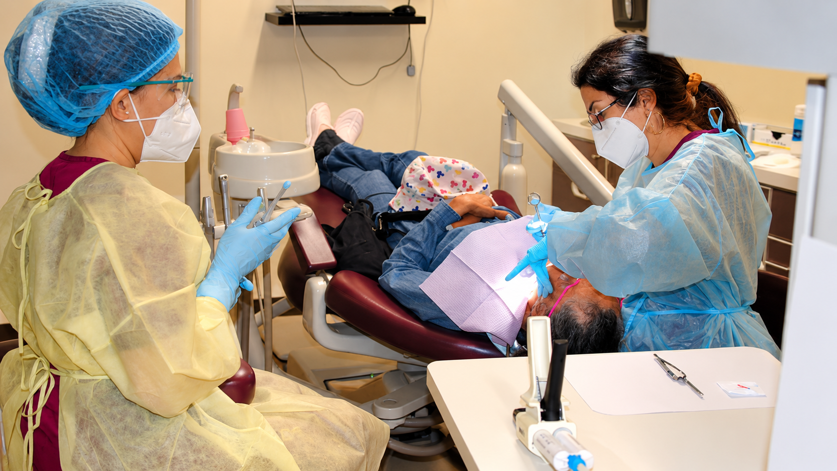 Dentist and assistant working on a patient in a dental clinic, both wearing masks and gloves