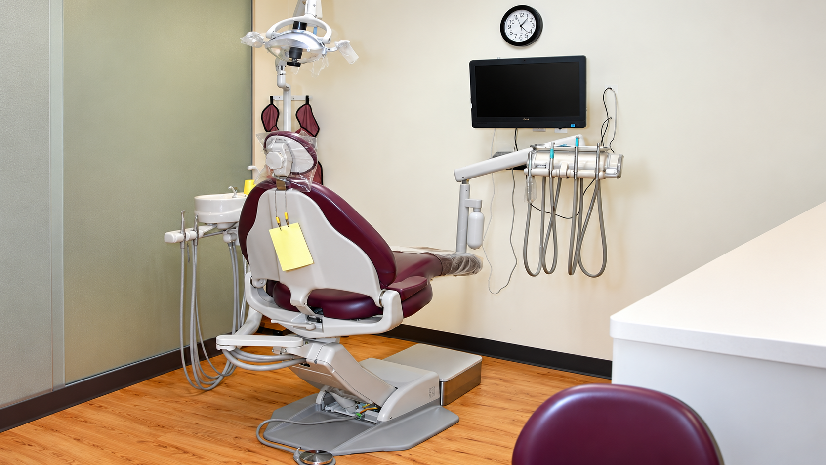 Dental exam room with maroon chair, monitor, tools, and wall clock