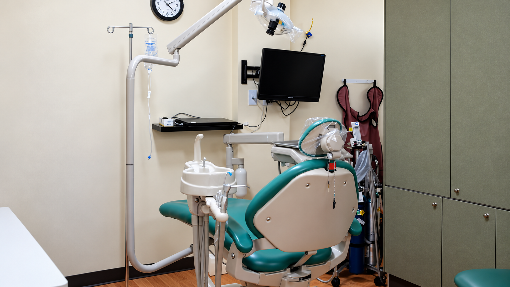 Dental exam room with turquoise chair, overhead light, monitor, and instruments