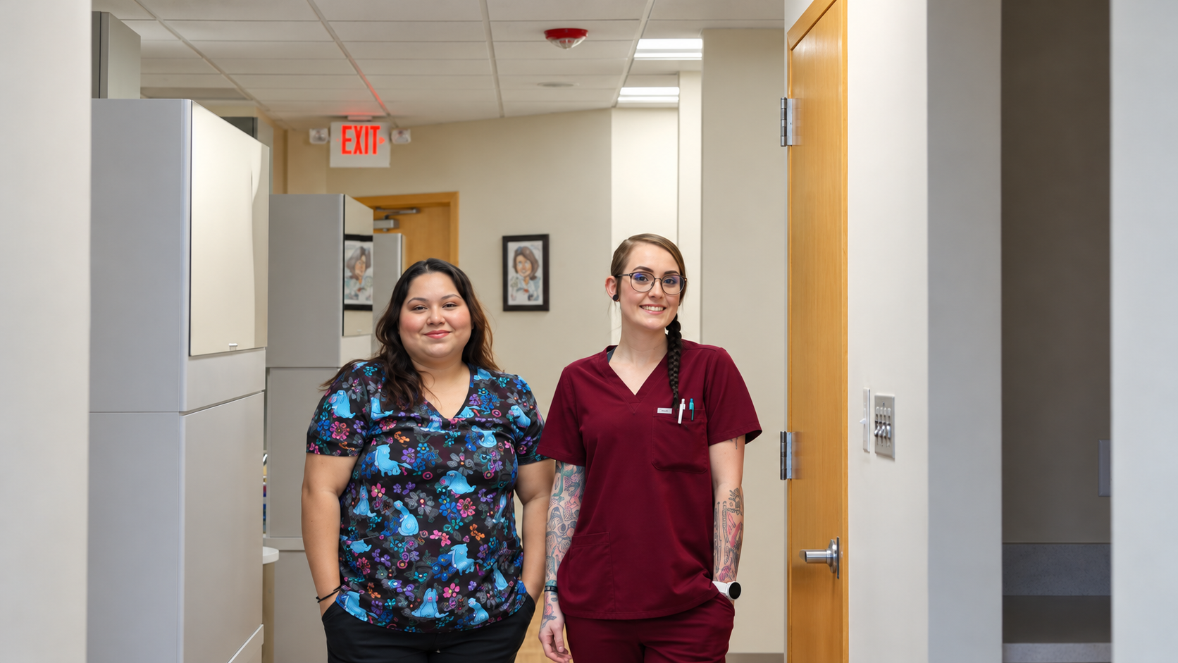 Two healthcare workers in scrubs walking down a hospital hallway