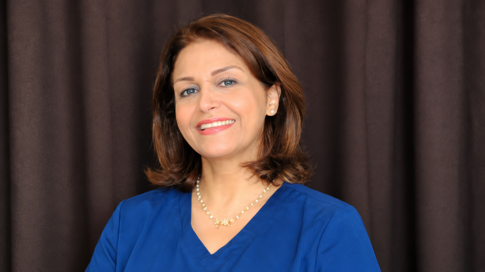 Woman in a blue blouse smiling in front of a dark curtain backdrop