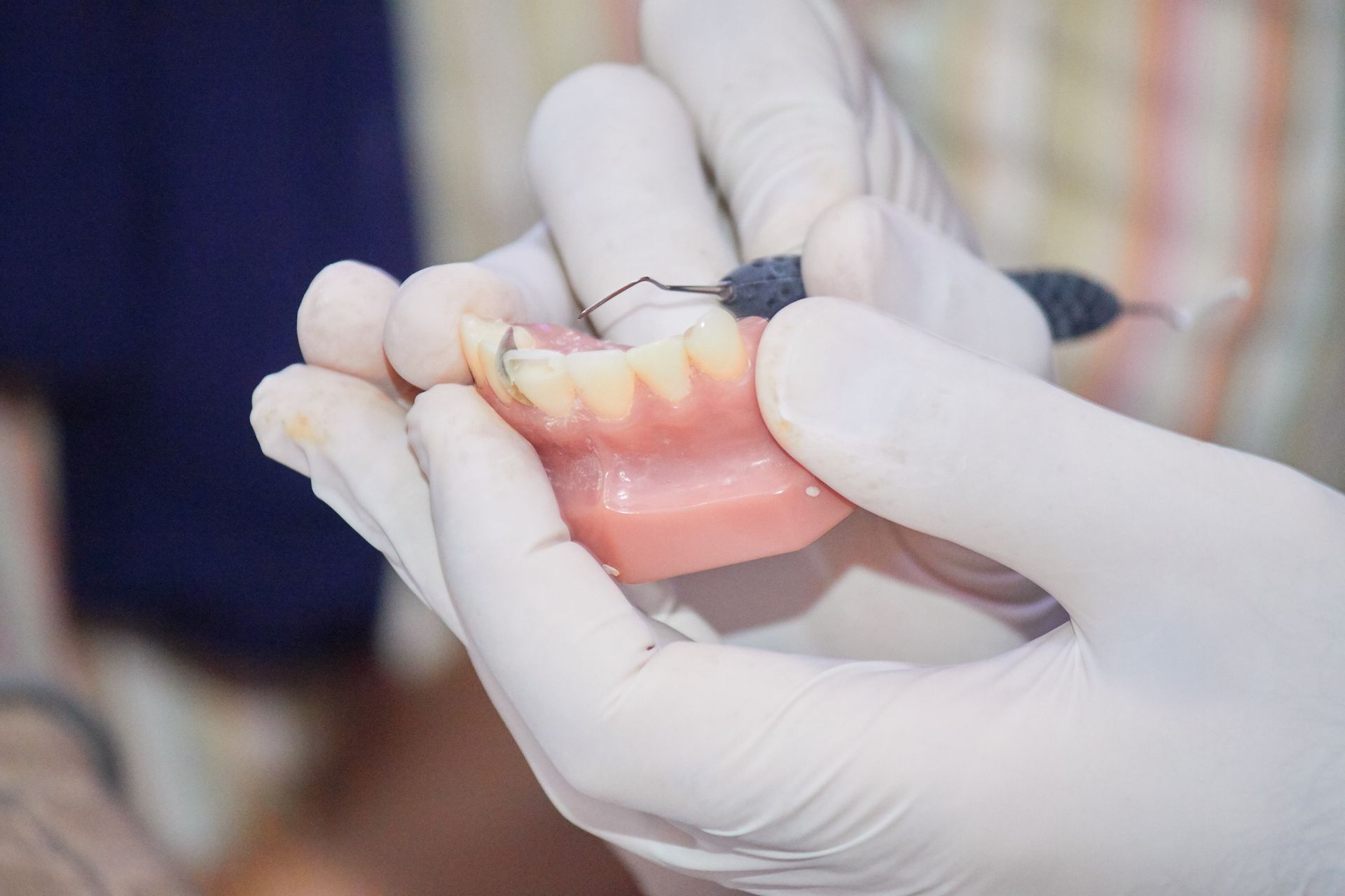 Photograph showing gloved hands holding a set of upper dentures with a dental tool being used for cleaning or adjustment.