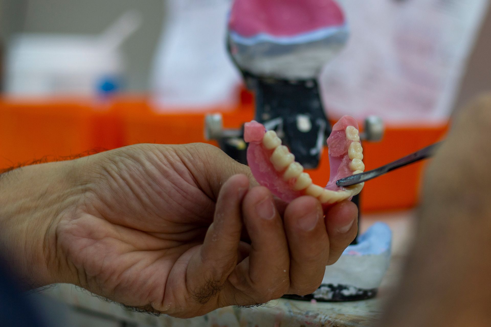 A denturist shaping denture teeth with a carving tool while holding a partial prosthesis in a lab A denturist shaping denture teeth with a carving tool while holding a partial prosthesis in a lab