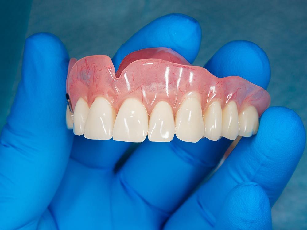 A blue-gloved individual displays a dental implant, highlighting custom dentures offered by Laney Dental & Denture Clinic in Edmonds, WA. A blue-gloved individual displays a dental implant, highlighting custom dentures offered by Laney Dental & Denture Clinic in Edmonds, WA.
