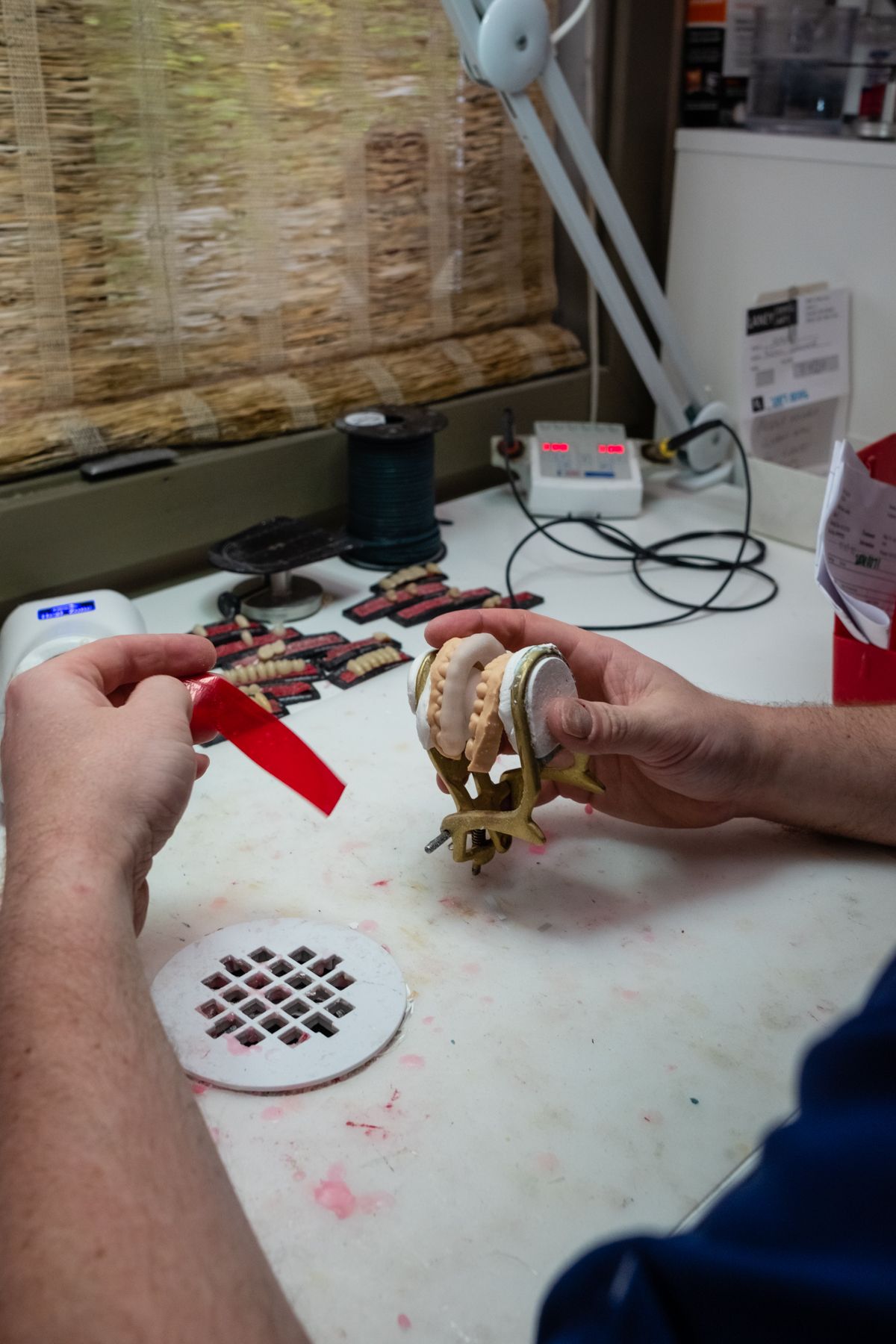 Person working on dental molds in a lab setting, holding a red tool and a model.