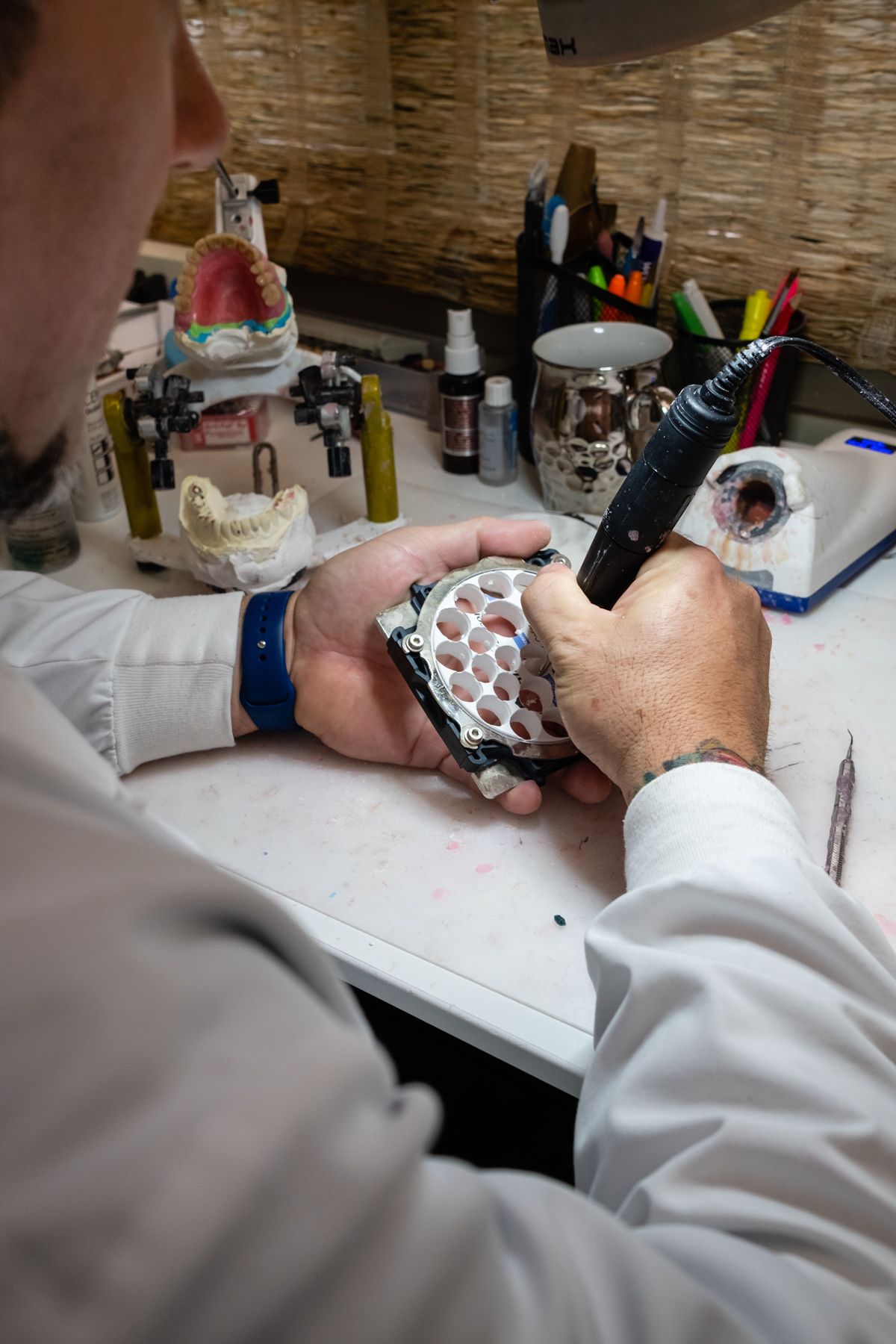 Person working on a dental mold, using a tool. Workspace includes other molds and tools on a white table.
