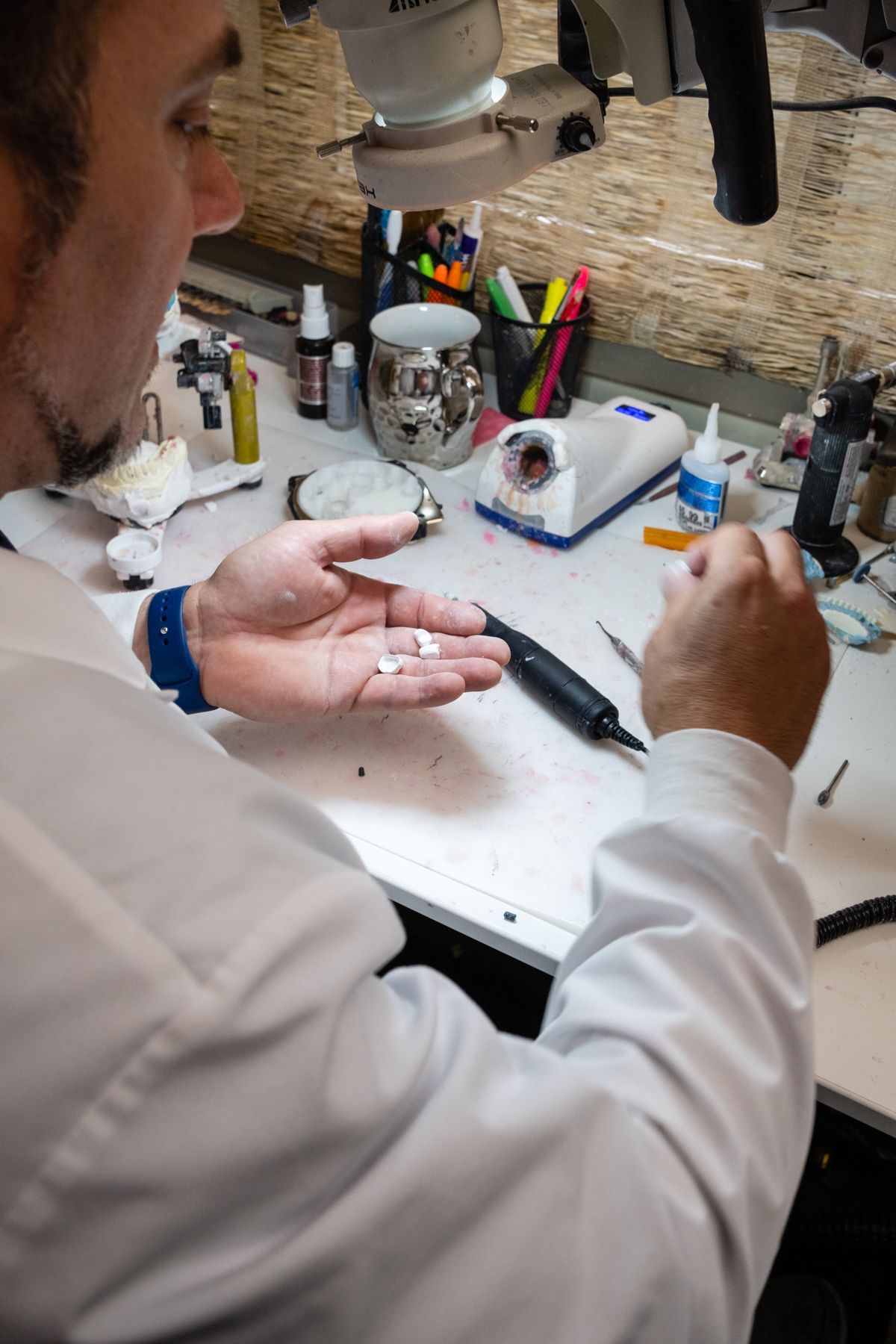 Person in lab coat holding small white objects, working at a table with equipment.