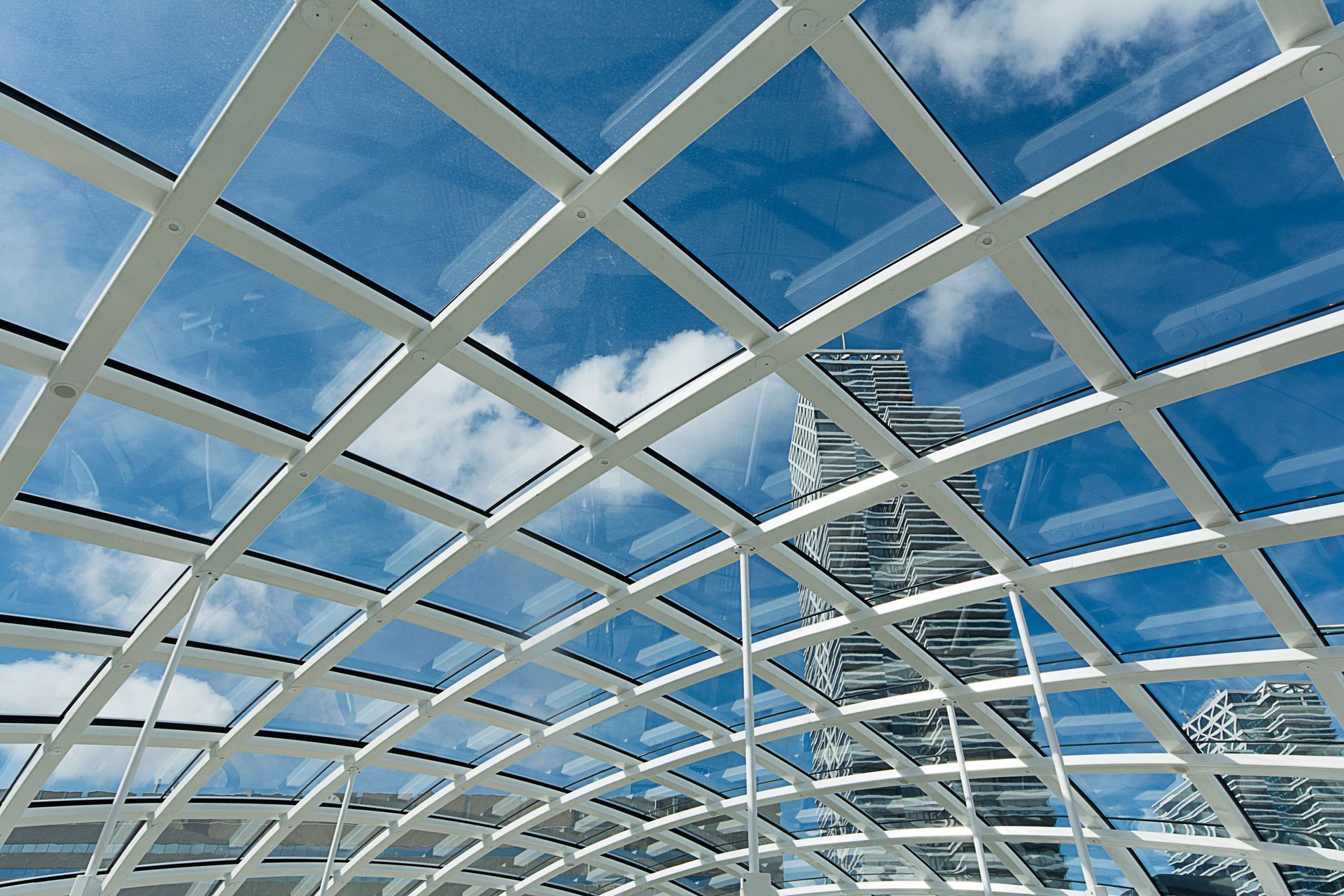White lattice roof framing a blue sky with clouds and modern buildings below