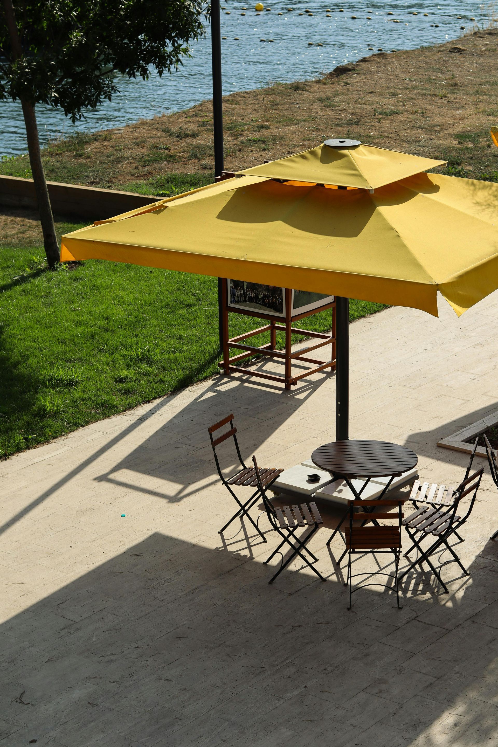 Patio table with chairs under a yellow umbrella beside a grassy waterfront.