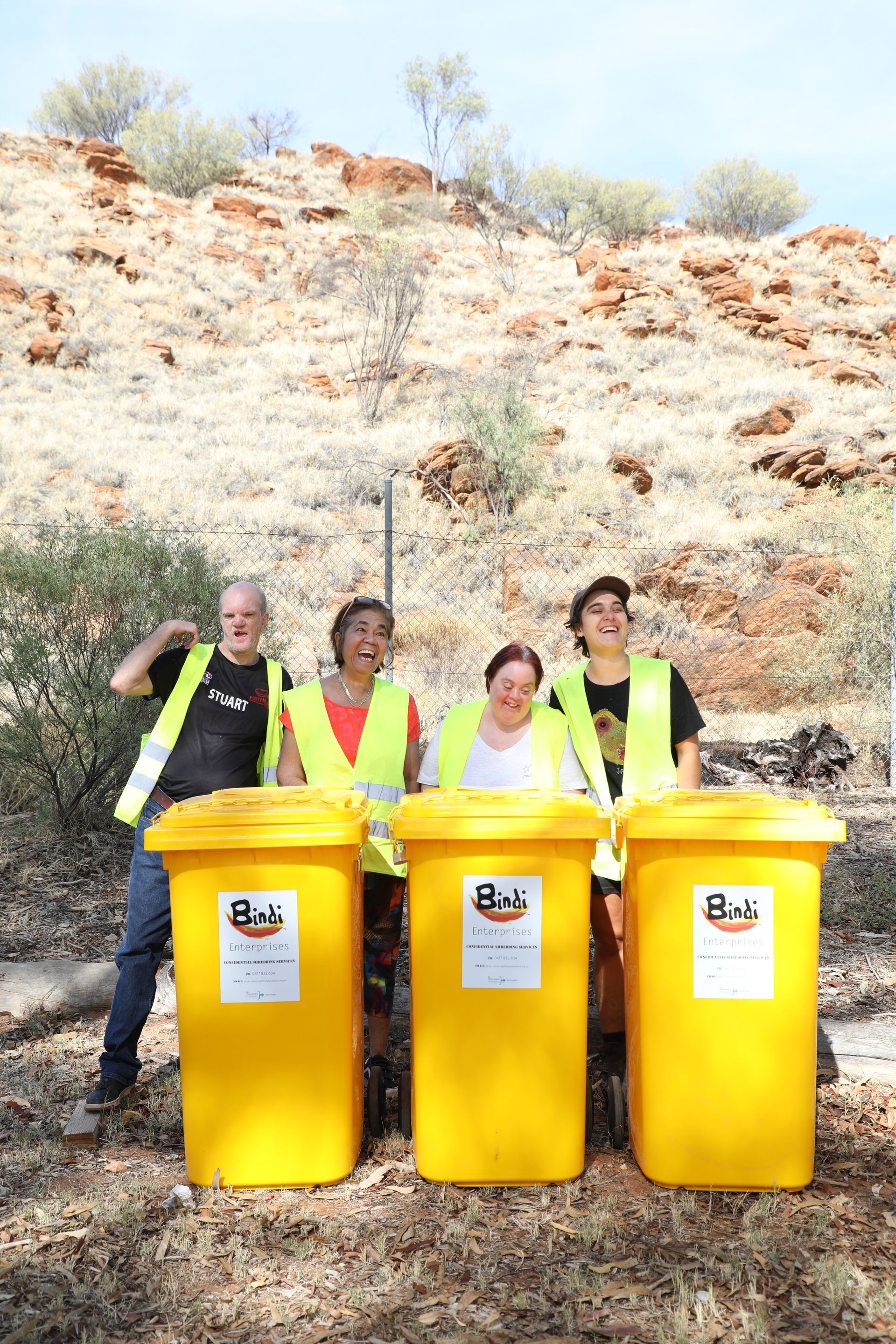 A group of people standing next to three yellow trash cans.