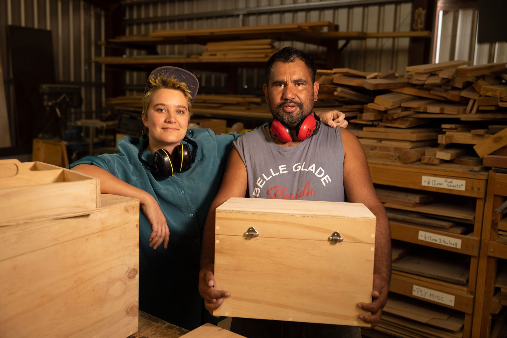 A man and a woman are holding a wooden box in a woodworking shop.