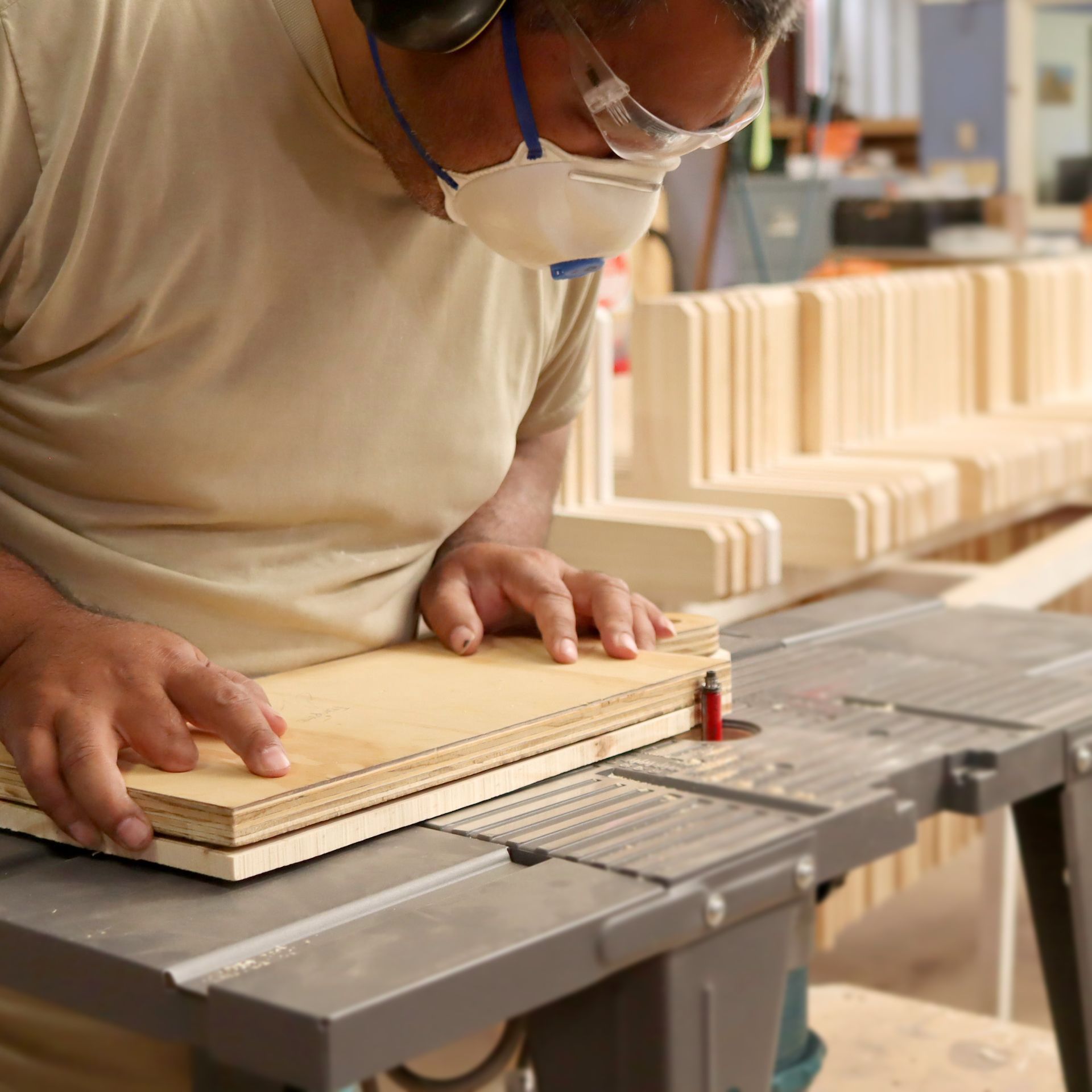 A man wearing a mask is cutting a piece of wood on a table saw