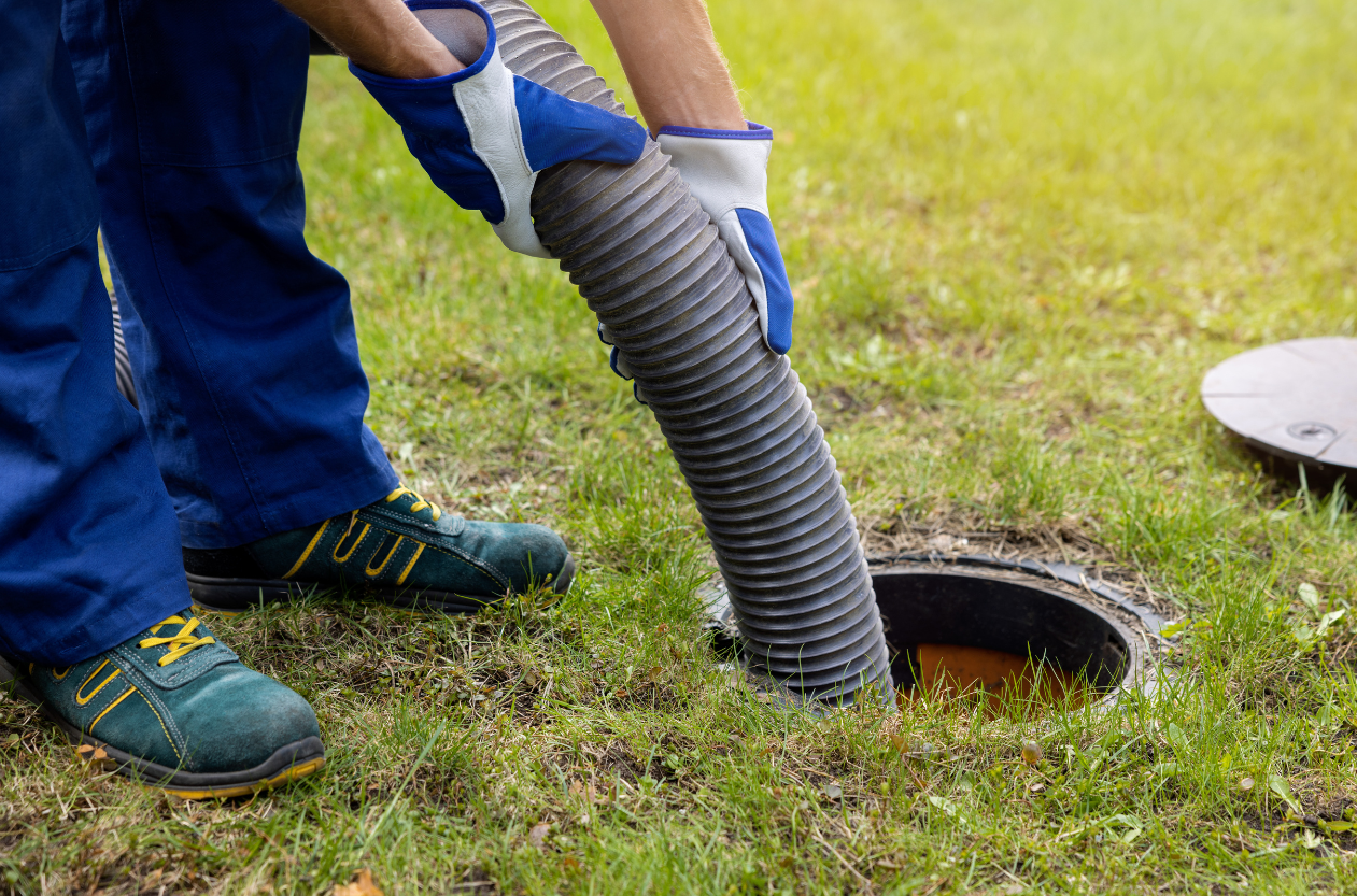 Person in blue coveralls pumping a septic tank with a hose in grassy area.