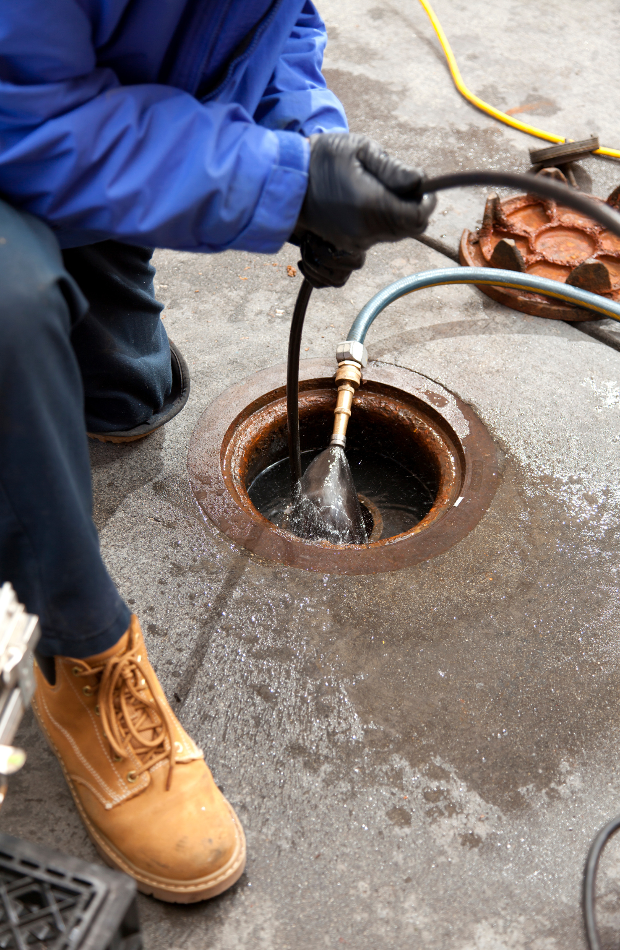 Person in blue coveralls and work boots cleaning a sewer drain.
