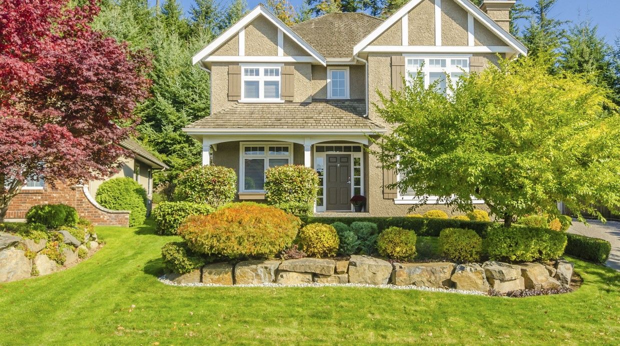 Suburban house with beige siding, stone accents, and a manicured front lawn and shrubs