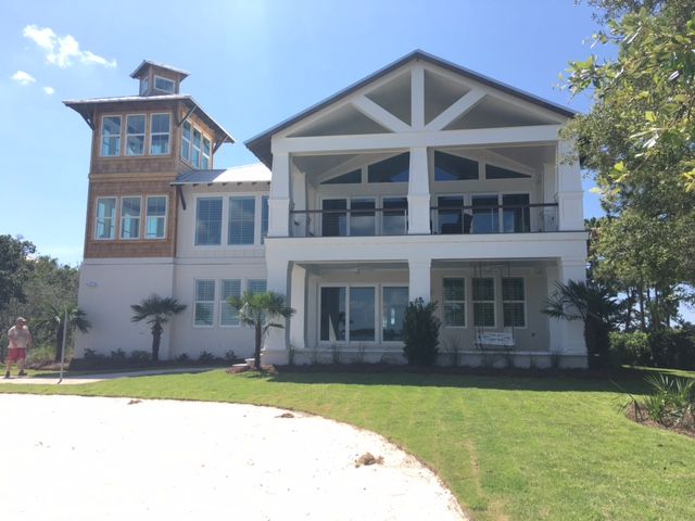Large white house with a brick tower and porch under a blue sky, with a green lawn in front