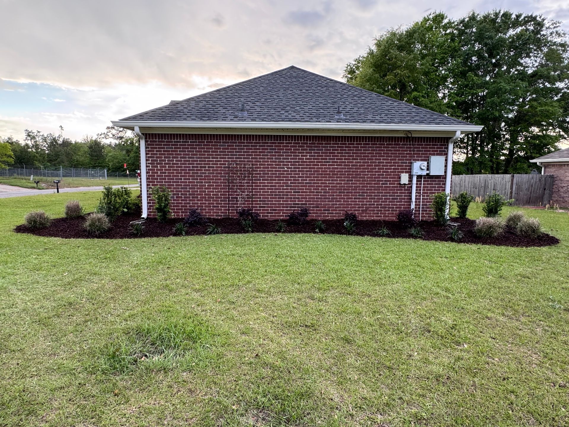 Small brick building with a shingled roof, surrounded by grass and landscaping.