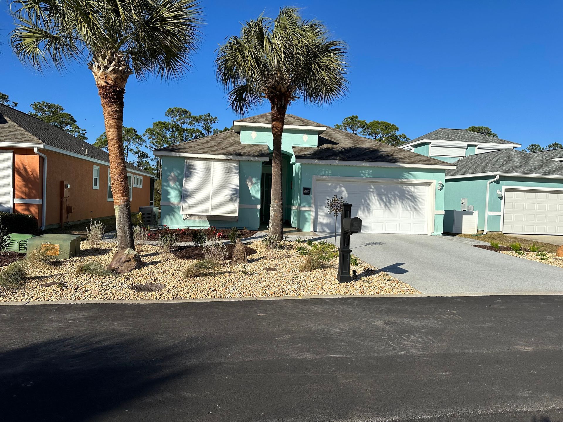 Single-story turquoise house with white garage and palm trees along a driveway under a clear blue sky