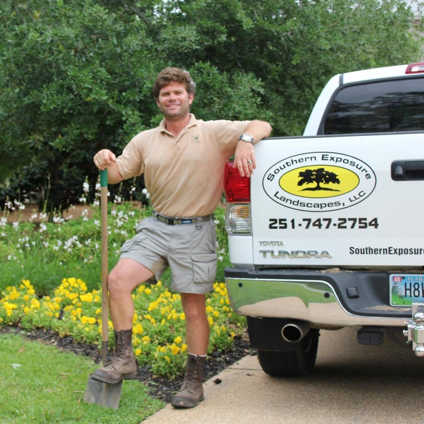 Man posing with shovel beside a landscaping truck and flower bed