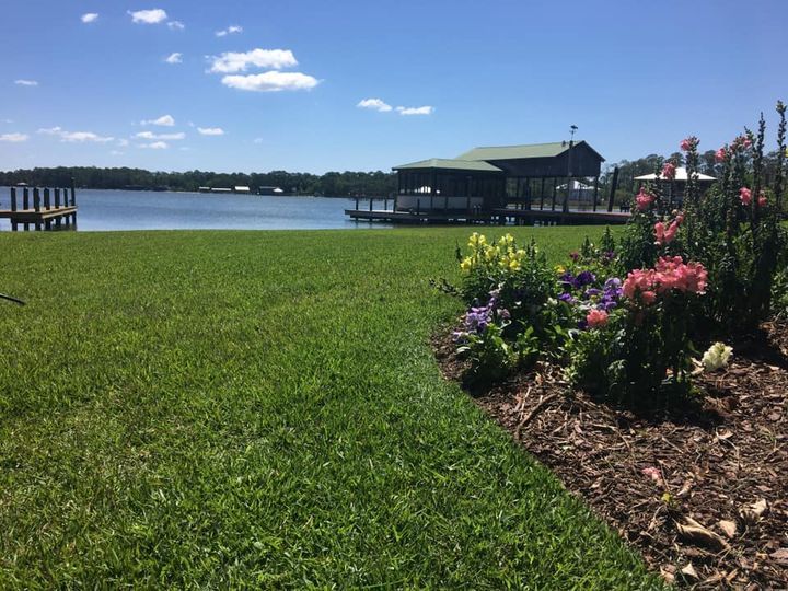 Lakeside lawn with flower bed, dock, and pavilion under a blue sky