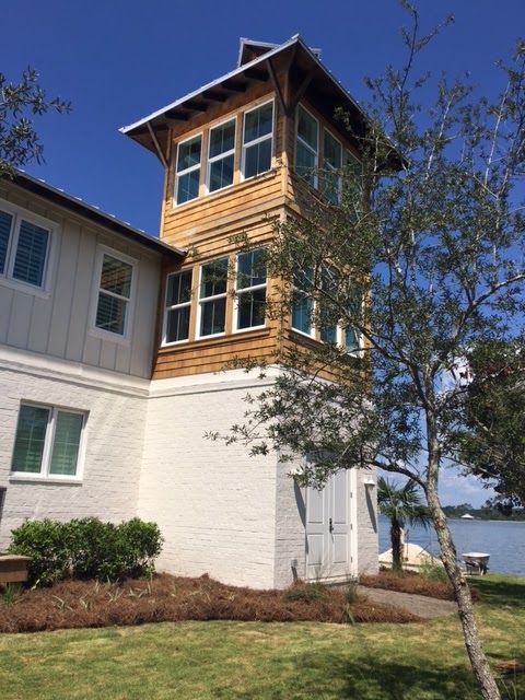 White brick and wood tower on a coastal building, with trees and water in the background.