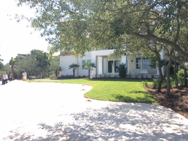 White house with green lawn and curved driveway under trees on a sunny day.