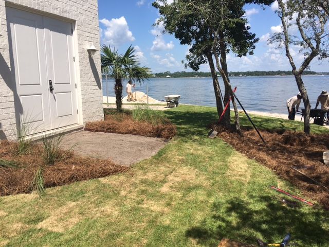 Lakeside yard with white building, grass, palm trees, and a dock by calm water