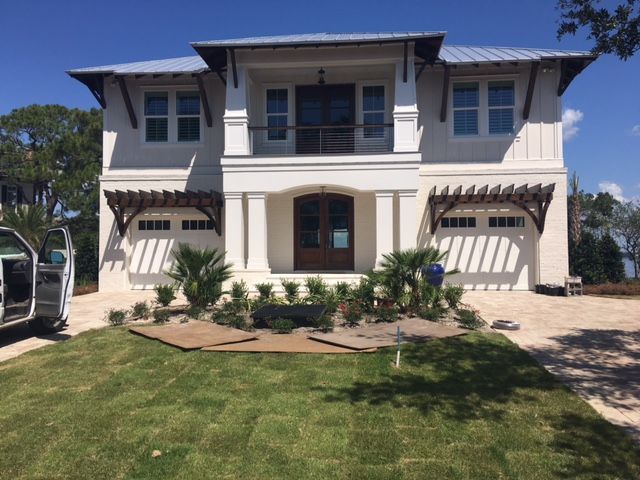 Two-story cream house with blue trim, front porch, and landscaped yard under a clear sky