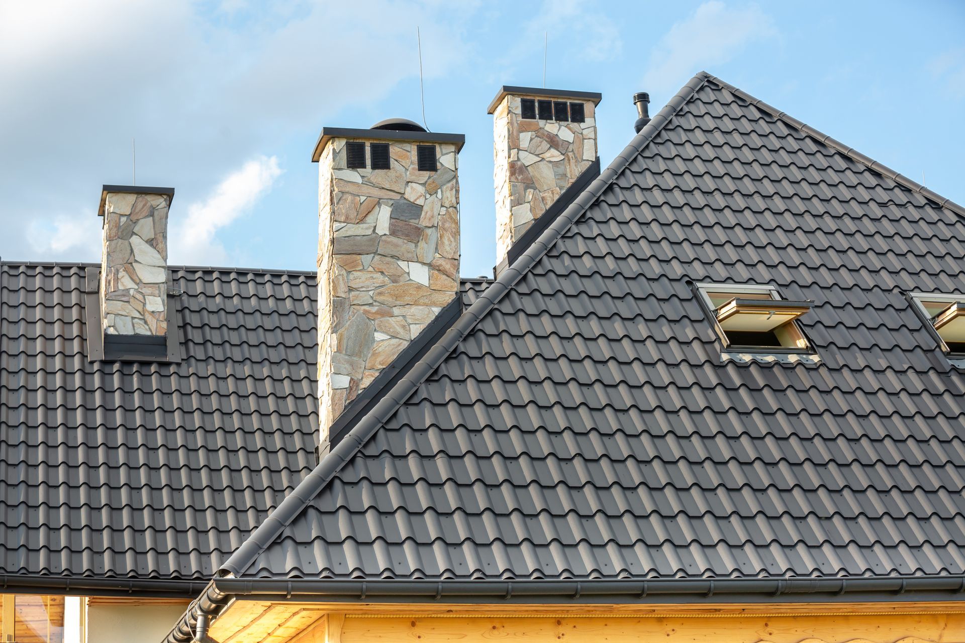 Modern tiled roof with three stone chimneys under a clear blue sky. Modern tiled roof with three stone chimneys under a clear blue sky.