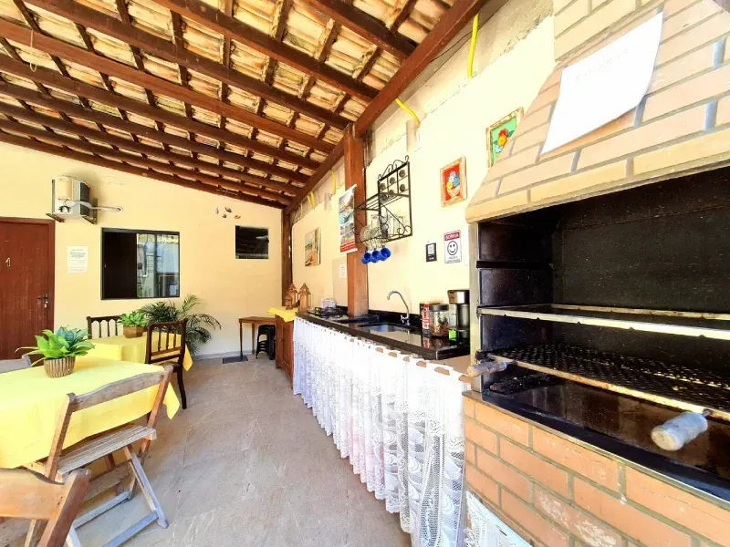 Um pátio externo coberto com uma mesa de jantar coberta com toalha amarela, um longo balcão de serviço e uma churrasqueira de carvão de tijolos.