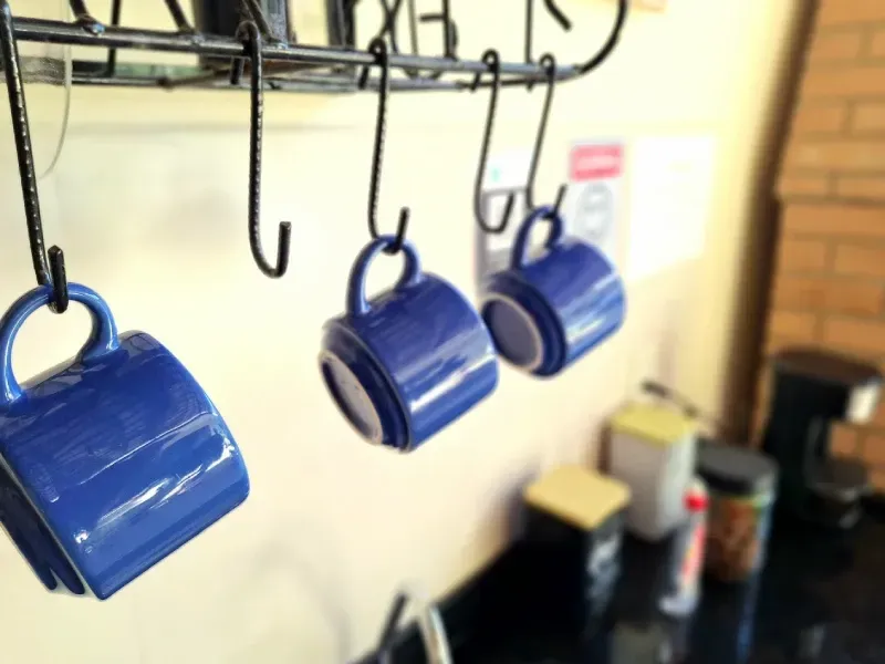 Três canecas de cerâmica azul estão penduradas em ganchos de metal preto acima da bancada da cozinha.