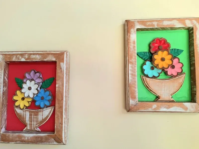 Duas molduras rústicas de madeira penduradas na parede, cada uma contendo uma colorida obra de arte floral em estilo 3D dentro de um vaso.