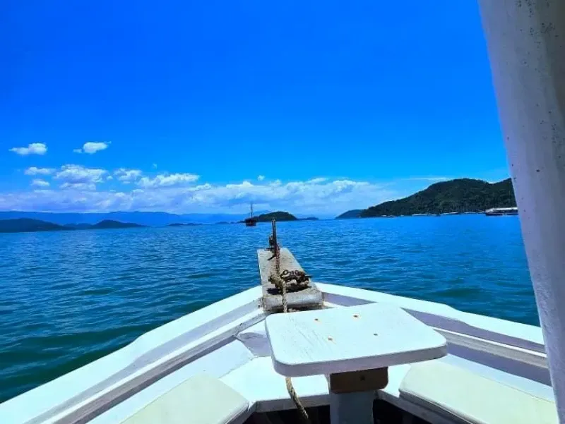 Vista da proa de um barco navegando em águas azuis calmas em direção a ilhas verdes distantes sob um céu claro.