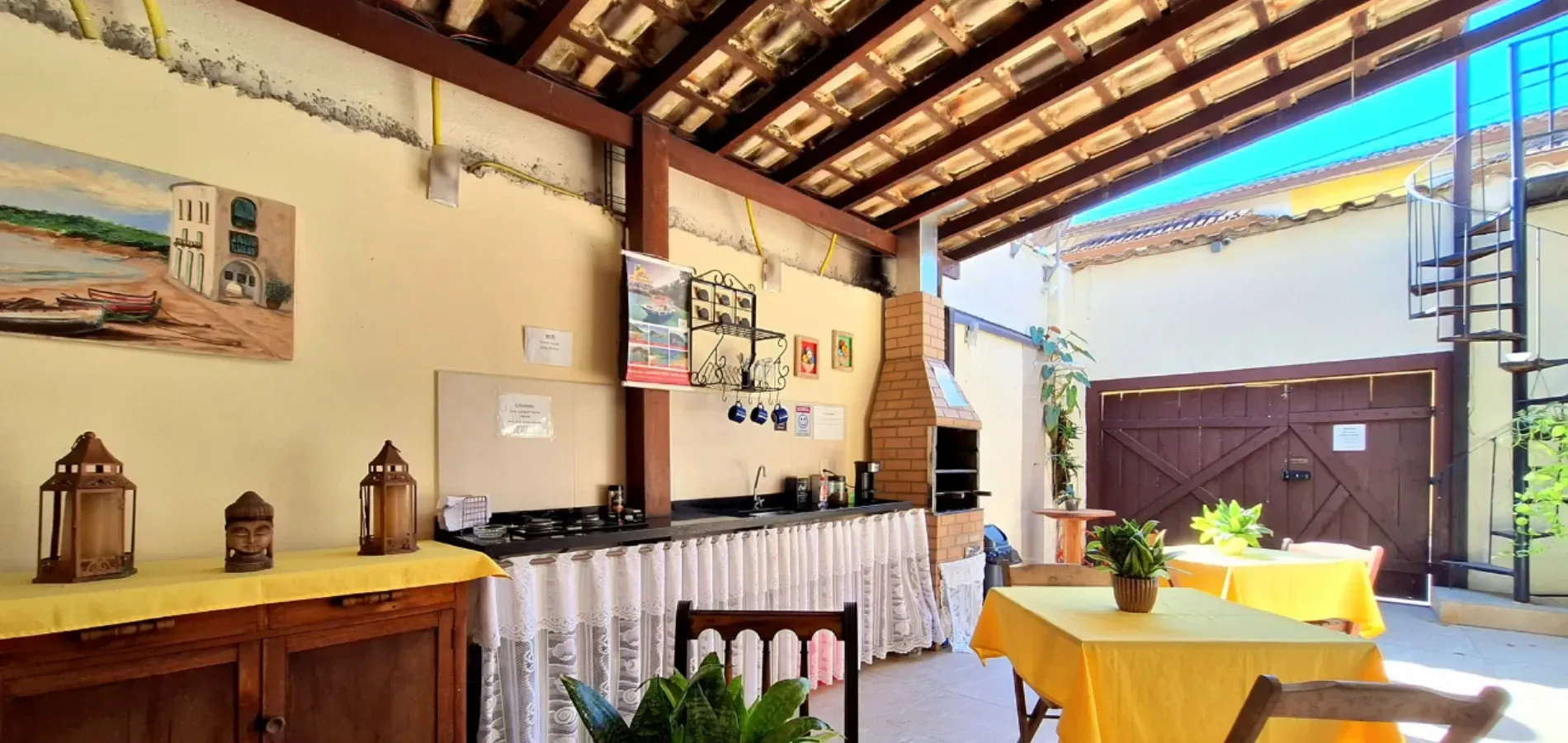 Um pátio com teto de madeira, churrasqueira de tijolos, balcões e mesas com toalhas de mesa amarelas.