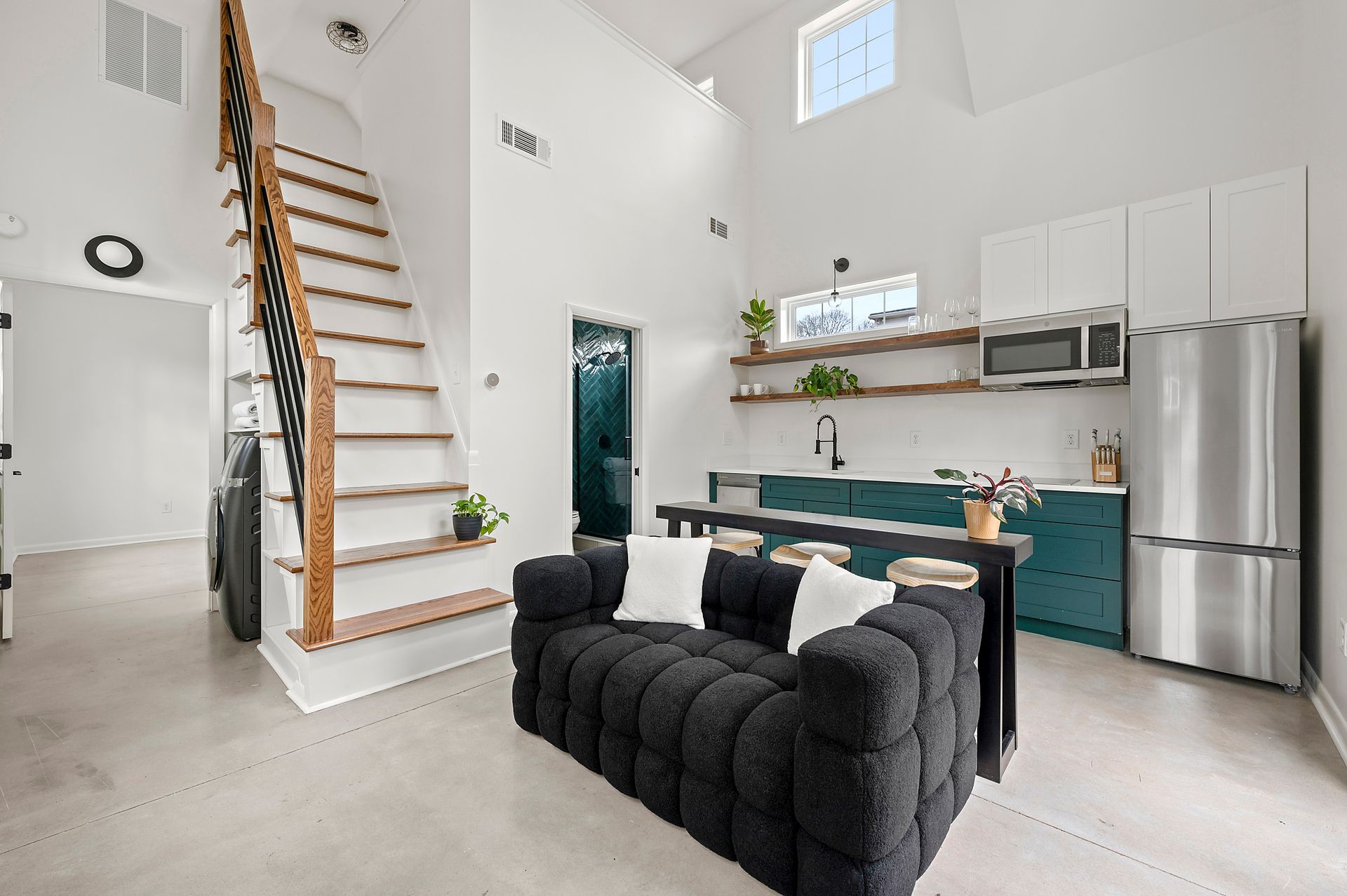 Modern loft interior with a kitchen, stairs, and a dark sofa.