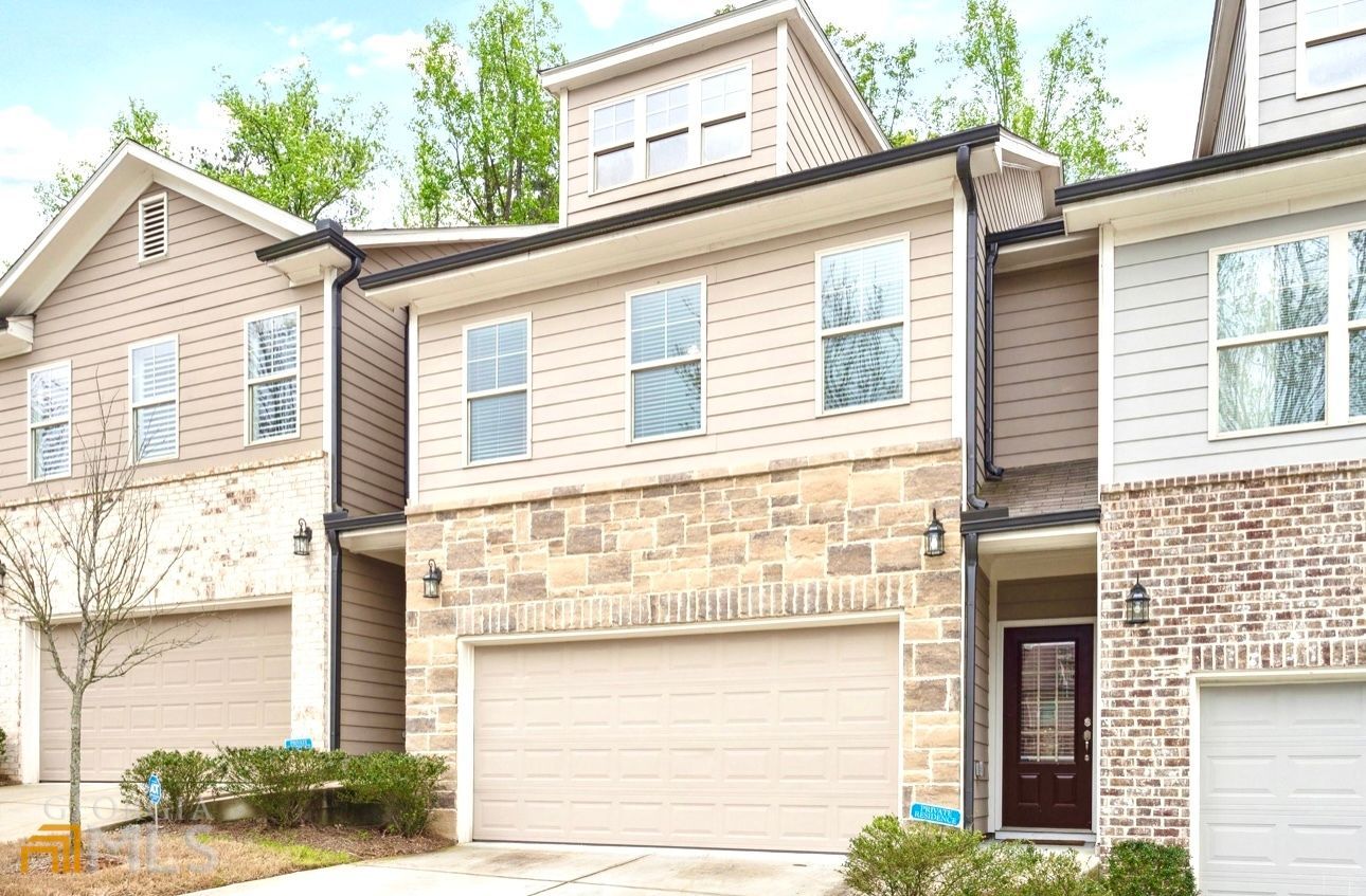 Row of townhouses with tan garage doors, stone accents, and brown front doors.