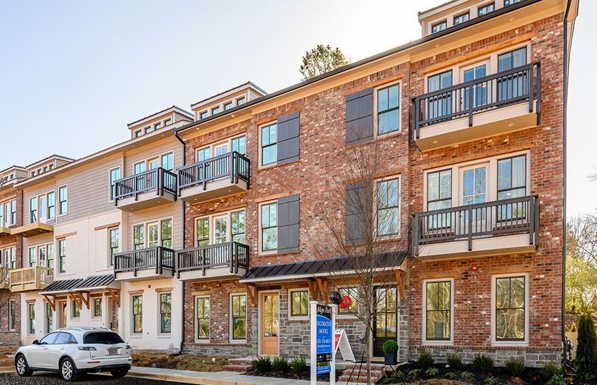 Red brick townhomes with balconies and dark shutters; white car parked in front.