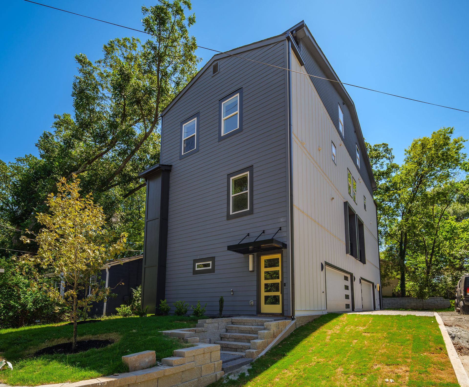 Modern gray multi-story house with yellow door and garage.