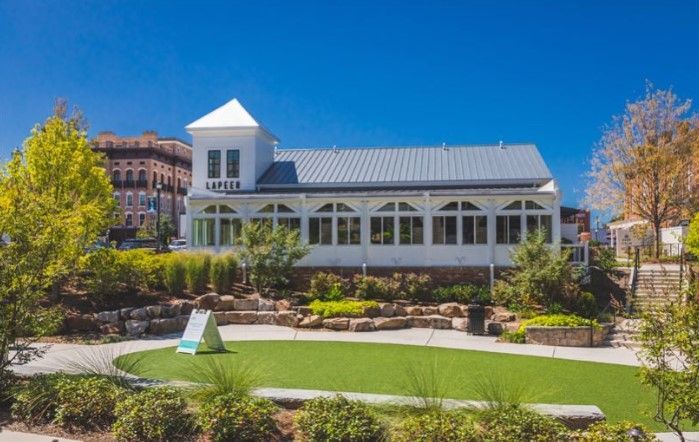 White building with a silver roof, situated by a green putting green and a walking path; bright blue sky.